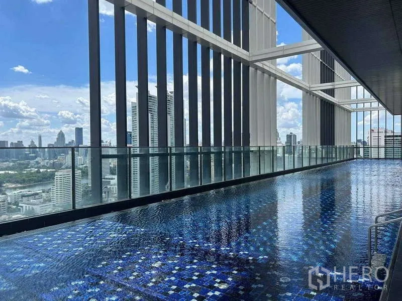 Condominium for rent or sale - Covered rooftop pool with mosaic tiles and panoramic Bangkok skyline views through glass balustrades.