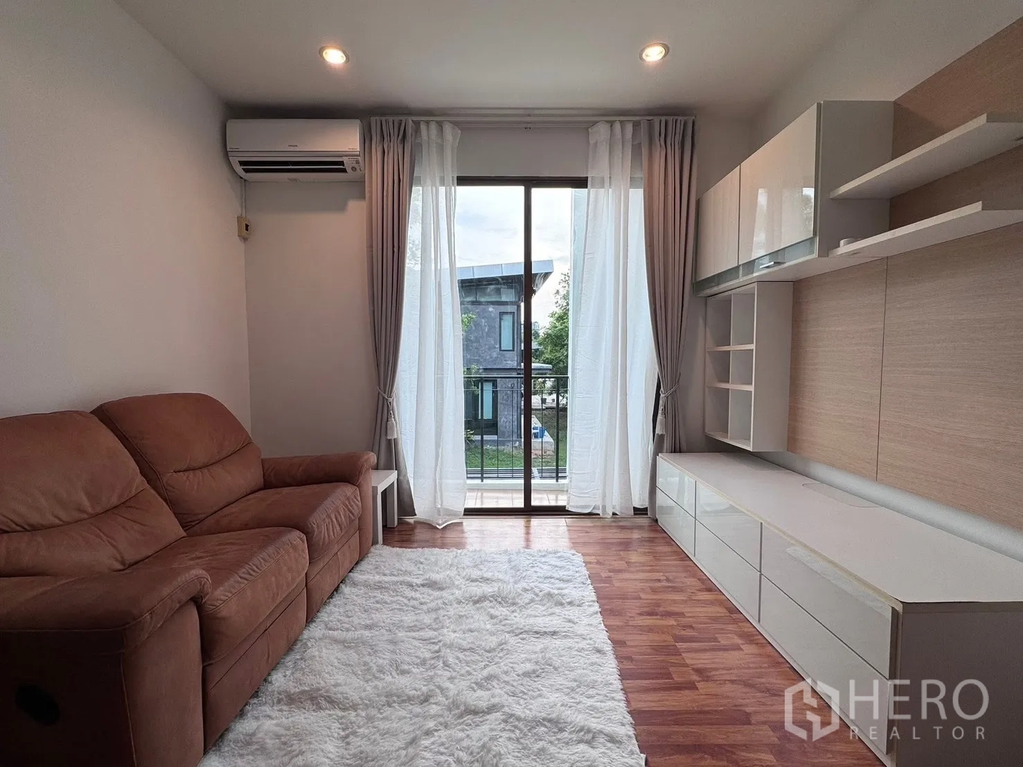 联排别墅 for rent in Phra Khanong, Bangkok - 客厅配内置电视柜与窗帘，旁为阳台门。