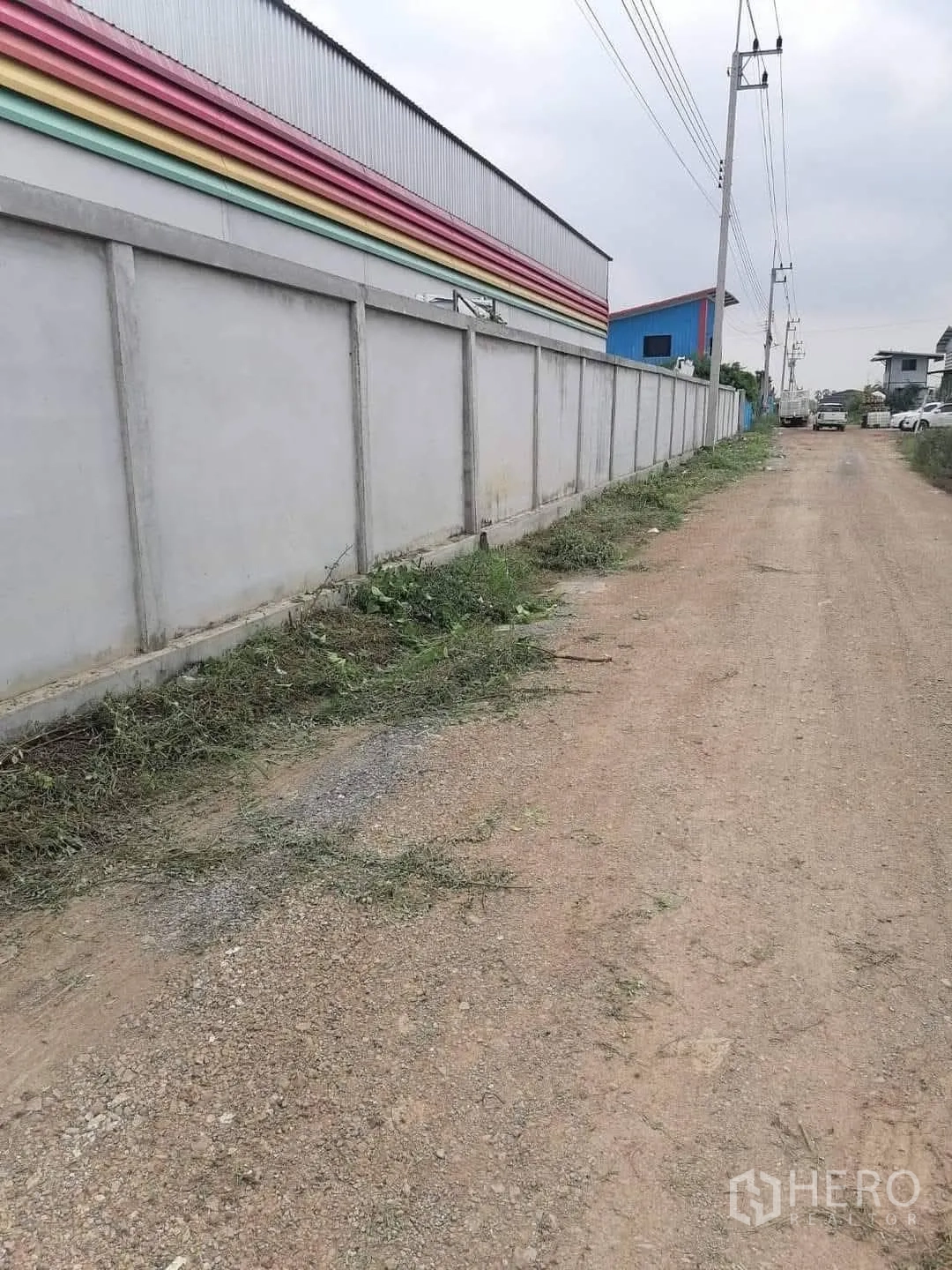 โกดัง for sale in Lam Luk Ka, Pathum Thani - ถนนลูกรังมีเสาไฟฟ้า ขนานกับกำแพงคอนกรีตรอบโกดัง