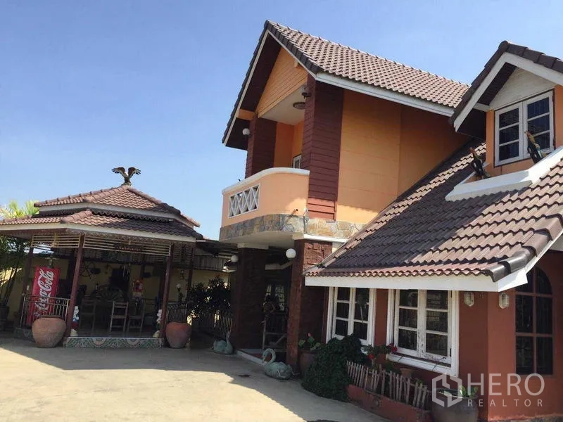 Detached House for rent or sale in Bang Bua Thong, Nonthaburi - Angle view of the house with a covered outdoor pavilion beside a wide paved courtyard.