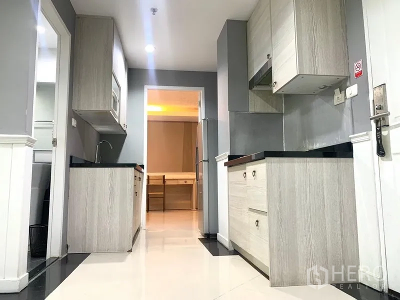 คอนโด ให้เช่าในKhlong Toei, Bangkok - โถงครัวสไตล์แกลเลย์ เคาน์เตอร์คู่และตู้ไม้โทนอ่อน เชื่อมต่อไปยังห้องนอน