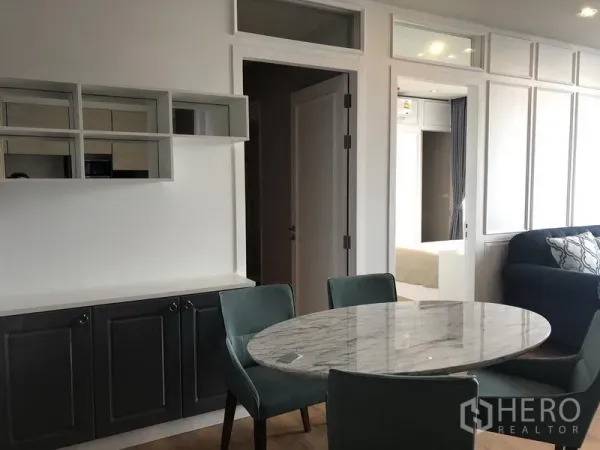 Condominium for rent in Khlong Toei, Bangkok - Dining corner with round marble table, teal chairs, and built-in cabinets.