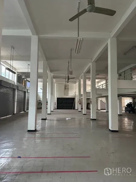店屋 出租在Khlong Toei, Bangkok - 店屋内部宽敞，挑高天花与成排立柱，吊扇、日光灯、瓷砖地面及多扇卷闸门。