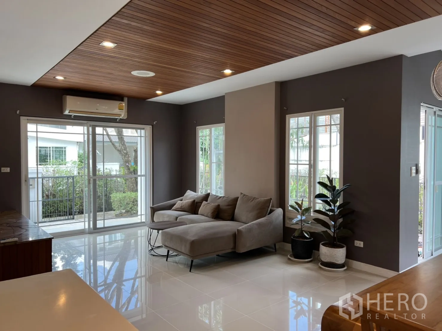 Detached House for rent in Bang Kapi, Bangkok - Air‑conditioned living area with sectional sofa, indoor plants, and sliding doors to the garden.