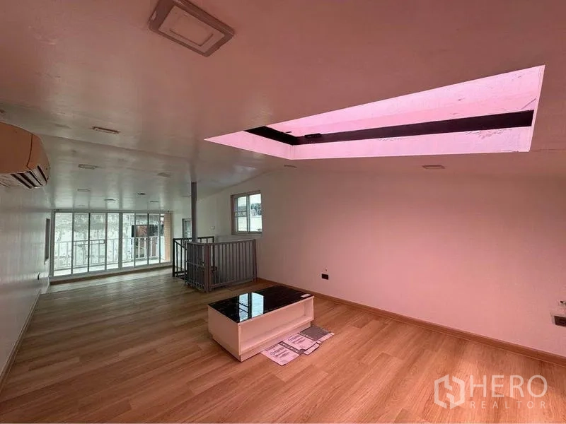 Shophouse for rent in Bang Rak, Bangkok - Open-plan top floor with skylight, light wood flooring, stairwell railing, and full-height windows.