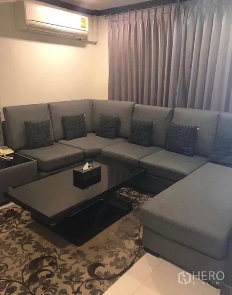 ทาวน์เฮาส์ ให้เช่าในKhlong Toei, Bangkok - ห้องนั่งเล่นอบอุ่น โซฟาเข้ามุมสีเทาขนาดใหญ่ ผ้าม่านทึบ แอร์ และโต๊ะกลางสีดำ