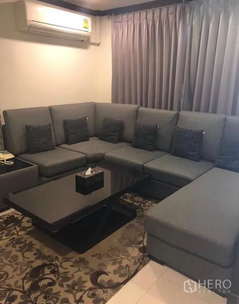 ทาวน์เฮาส์ ให้เช่าในKhlong Toei, Bangkok - ห้องนั่งเล่นอบอุ่น โซฟาเข้ามุมสีเทาขนาดใหญ่ ผ้าม่านทึบ แอร์ และโต๊ะกลางสีดำ