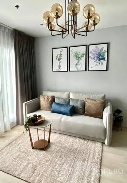Condominium for rent in Pathum Wan, Bangkok - Compact lounge with sofa, round coffee table, rug and statement chandelier.