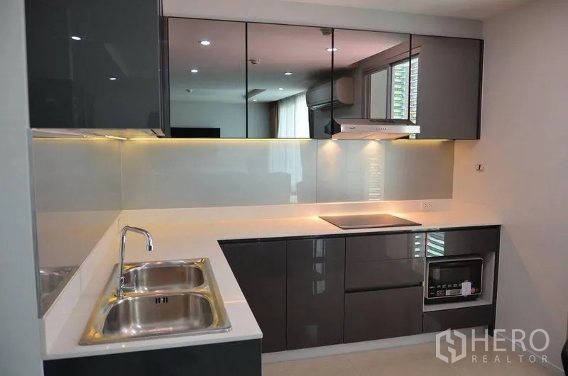 Condominium for rent in Watthana, Bangkok - L-shaped modern kitchen with glossy gray cabinets, double sink, electric cooktop and under-cabinet lighting.