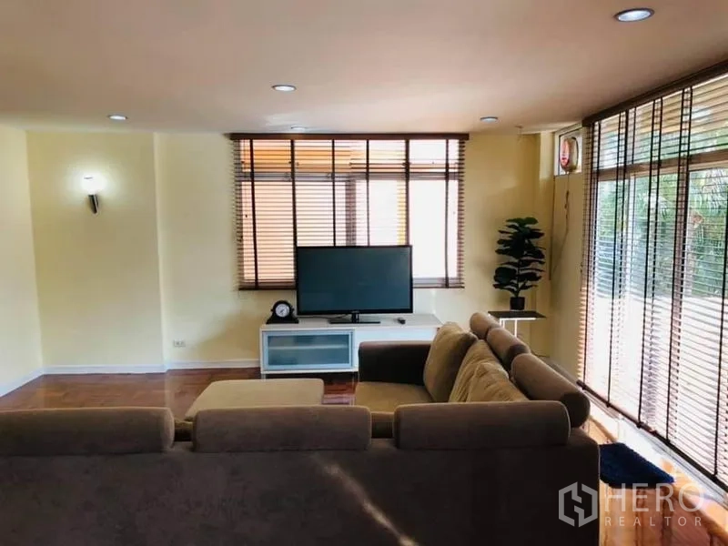Detached House for rent in Watthana, Bangkok - Spacious media room with large windows, blinds, TV stand, and recessed lighting.