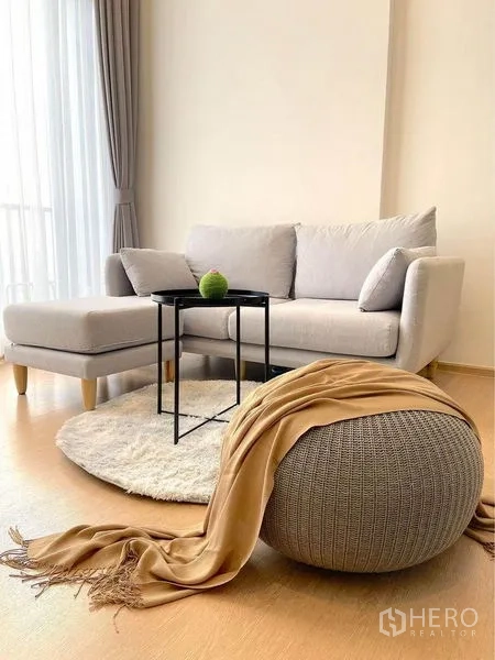 Condominium for rent in Watthana, Bangkok - Cozy living area with light-gray L-shaped sofa, round rug, and nesting side tables.
