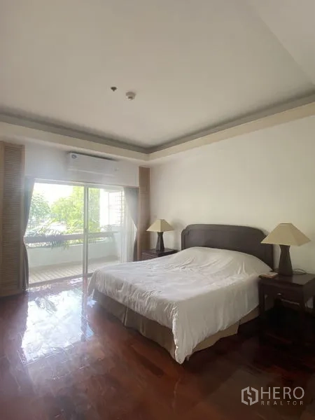 Condominium for rent - Primary bedroom with large bed, bedside tables, wood floors and sliding door to a green-view balcony.