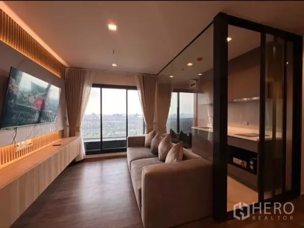 Condominium for rent in Chatuchak, Bangkok - Living area with wall-mounted TV, large sofa, and panoramic city view from the balcony.