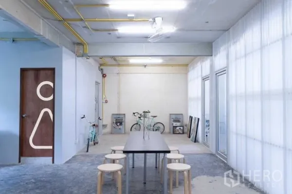 办公空间 出租在Phaya Thai, Bangkok - 开放工作区，两张白色桌子置于工业风天花下，自然光充足的全景窗。