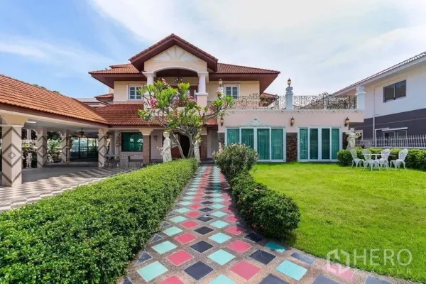 独立式住宅 出租或出售在Bang Khen, Bangkok - 彩色地砖小径通向两层独栋住宅，红瓦屋顶、阳台、庭院雕像与大面积草坪。