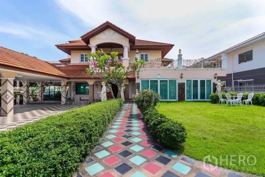 独立式住宅 出租或出售在Bang Khen, Bangkok - 彩色地砖小径通向两层独栋住宅，红瓦屋顶、阳台、庭院雕像与大面积草坪。