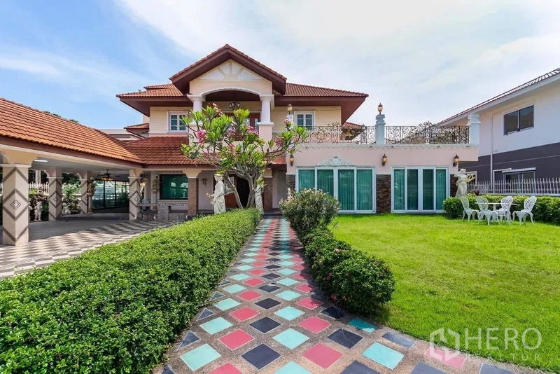 独立式住宅 出租或出售在Bang Khen, Bangkok - 彩色地砖小径通向两层独栋住宅，红瓦屋顶、阳台、庭院雕像与大面积草坪。