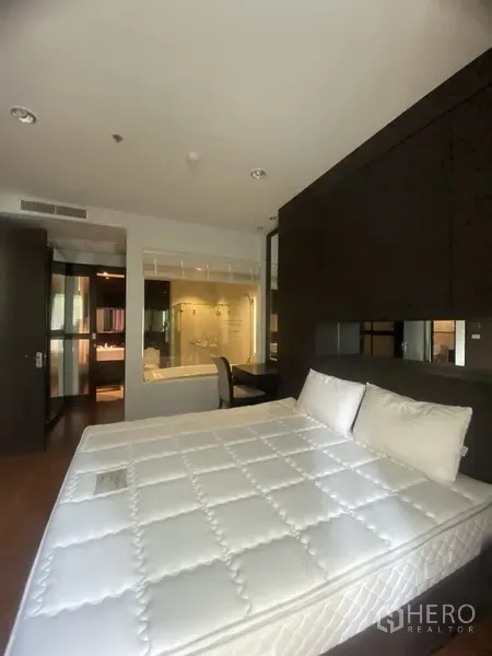 คอนโด ให้เช่าในPathum Wan, Bangkok - ห้องนอนหลักพร้อมเตียงใหญ่ ฉากกั้นบิวท์อิน โต๊ะทำงาน และห้องน้ำในตัวผนังกระจกพร้อมอ่างล้างหน้า