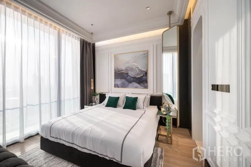 Condominium for rent in Bang Rak, Bangkok - Sunlit bedroom with king bed, artwork and sheer curtains opening to a city balcony.
