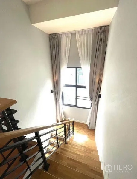 Detached House for rent - Staircase with wooden steps, black metal railing and a tall window draped with light curtains.