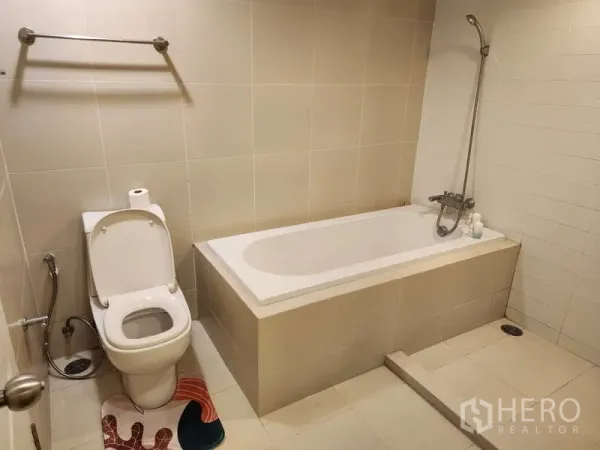Condominium for rent in Huai Khwang, Bangkok - Bathroom with built-in bathtub, handheld shower and toilet finished in beige tiles.