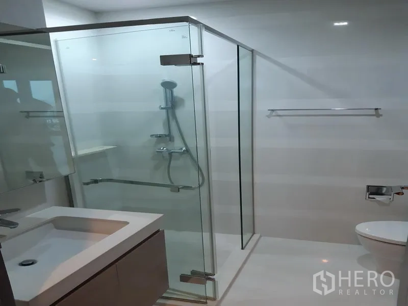 Condominium for rent in Khlong Toei, Bangkok - Bright bathroom with glass-enclosed shower and vanity.