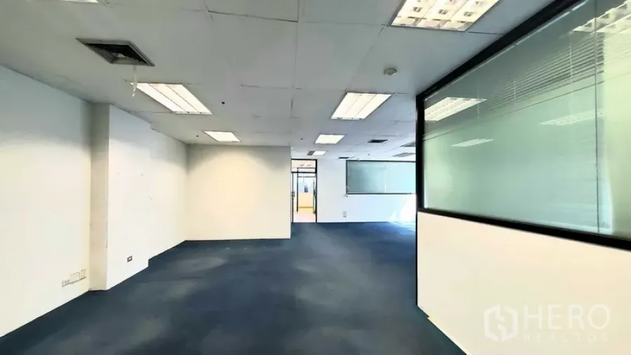 Office Space for rent in Khlong Toei, Bangkok - Open-plan office with blue carpet, drop-ceiling lights, and an interior glass partition.