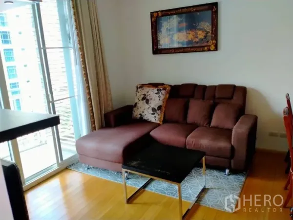 คอนโด ให้เช่าในWatthana, Bangkok - ห้องนั่งเล่นสว่าง โซฟาเข้ามุมสีน้ำตาล โต๊ะกลาง และประตูกระจกบานเลื่อนเปิดสู่ระเบียงในคอนโดกรุงเทพฯ