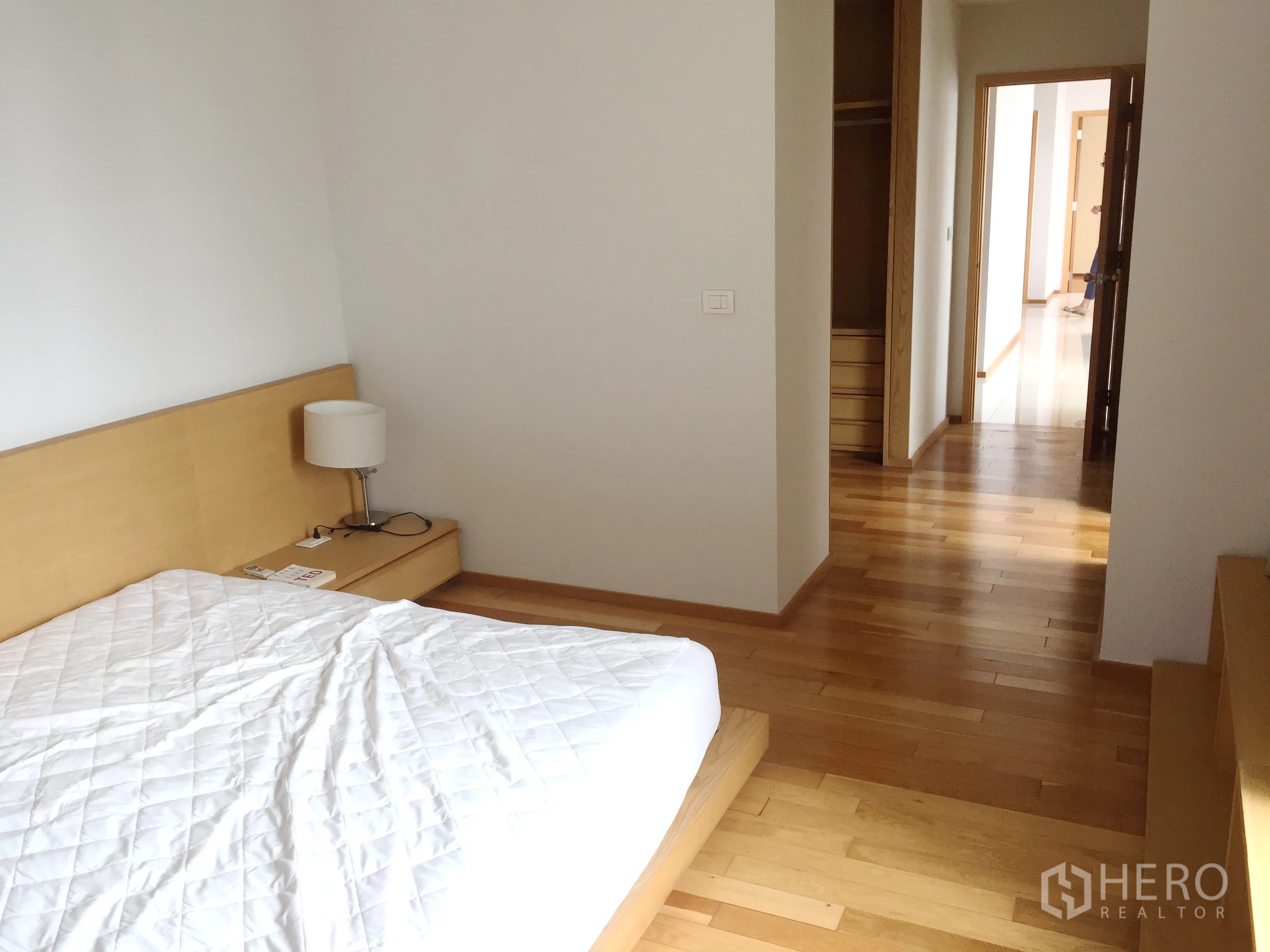 คอนโด ให้เช่าในKhlong Toei, Bangkok - ห้องนอนมินิมอล เตียงแพลตฟอร์ม โต๊ะหัวเตียง และโถงทางเดินสู่ตู้เสื้อผ้าบิวท์อิน พื้นไม้