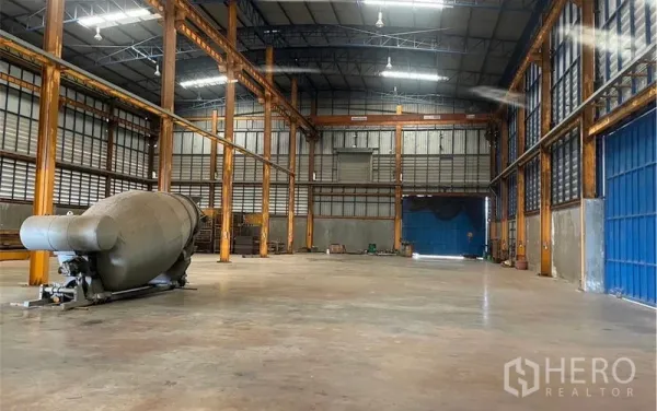 Factory for rent in Samut Songkhram - High-ceiling steel-frame factory interior with orange columns, polished concrete floor, blue roller door and an industrial tank.
