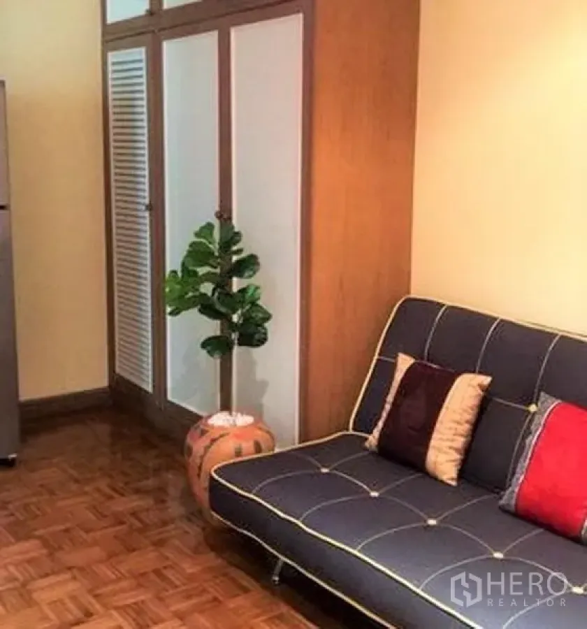 คอนโด ให้เช่าในSathon, Bangkok - มุมนั่งเล่น โซฟาสีน้ำเงินหมอนอิงหลากสี ข้างตู้เสื้อผ้า ตู้เย็น และต้นไม้กระถาง