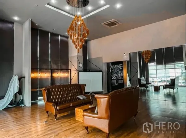 Office Space for rent in Lak Si, Bangkok - Spacious office area with two brown leather sofas, statement chandelier, floor-to-ceiling windows, projector screen and mirrored panels.