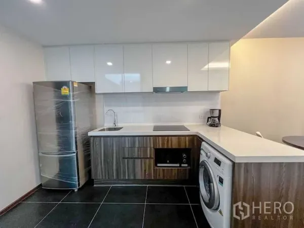 Condominium for sale in Huai Khwang, Bangkok - L-shaped kitchen with glossy cabinets, electric hob, oven, refrigerator and a front-loading washing machine.