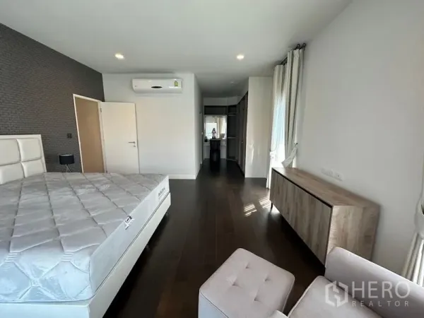 บ้าน ให้เช่าหรือขายในLam Luk Ka, Pathum Thani - ห้องนอนมาสเตอร์กว้าง พื้นไม้ เตียงสีขาว เครื่องปรับอากาศ และทางเข้าห้องแต่งตัว