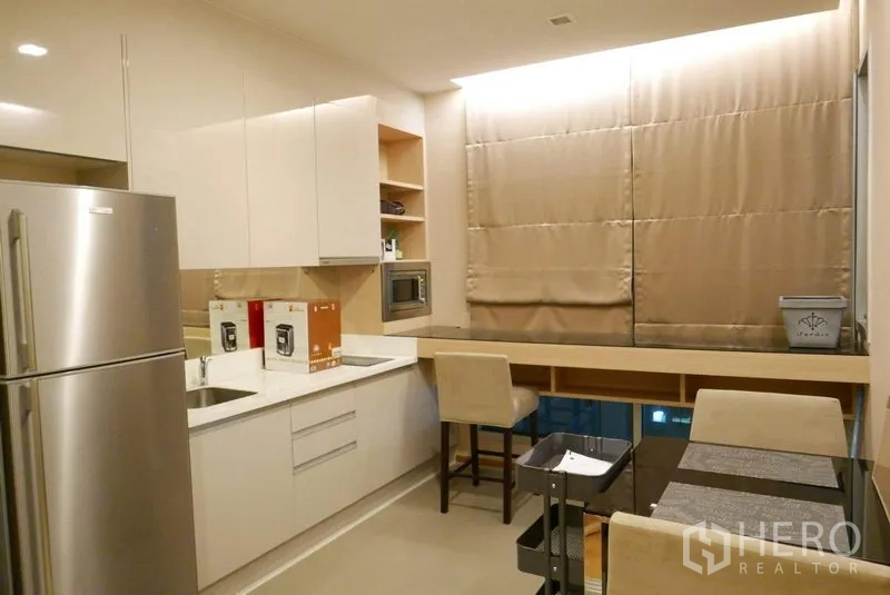 Condominium for rent in Ratchathewi, Bangkok - Modern kitchen with white cabinets, stainless refrigerator, built-in microwave and a dining counter for two.