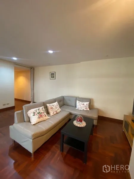 คอนโด ให้เช่าในPathum Wan, Bangkok - ห้องนั่งเล่นอบอุ่น โซฟารูปตัวแอล โต๊ะกลาง และชั้นวางทีวี บนพื้นปาร์เกต์