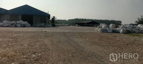 โรงงาน ขายในPhanat Nikhom, Chon Buri - ลานโล่งขนาดใหญ่รอบอาคารโรงงานเตี้ย ๆ มีถุงวัสดุกองอยู่หลายจุด.