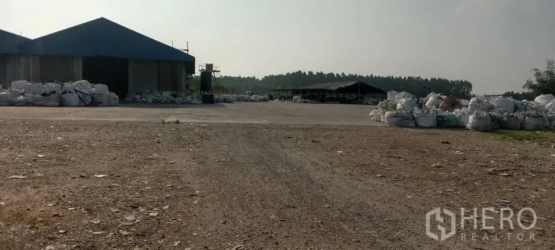 โรงงาน ขายในPhanat Nikhom, Chon Buri - ลานโล่งขนาดใหญ่รอบอาคารโรงงานเตี้ย ๆ มีถุงวัสดุกองอยู่หลายจุด.