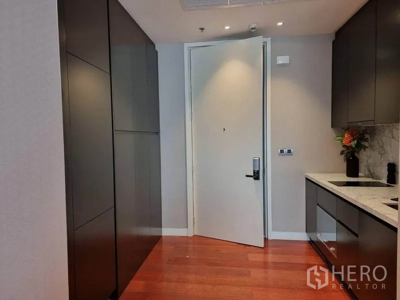 公寓 出租在Watthana, Bangkok - 入户走廊配嵌入式柜体与小厨房，木地板与白色入户门。