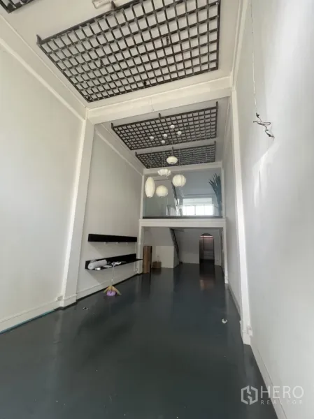 店屋 出租或出售在Watthana, Bangkok - 店屋底层挑空大厅，网格吊顶与深色环氧地坪、展示搁板。