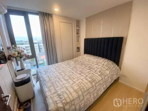 คอนโด ขาย - ห้องนอนอบอุ่นพร้อมหัวเตียงบุและชั้นวางมุมกับหน้าต่างรับวิวเมือง