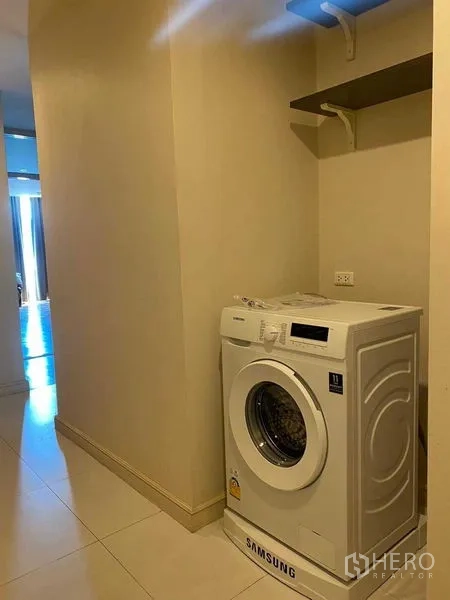 Condominium for rent in Pathum Wan, Bangkok - Laundry alcove with a front-loading washing machine and wall shelves.