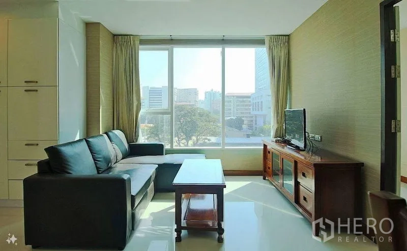 Condominium for sale in Watthana, Bangkok - Living room with sofa and TV stand facing wide windows with park and skyline views.
