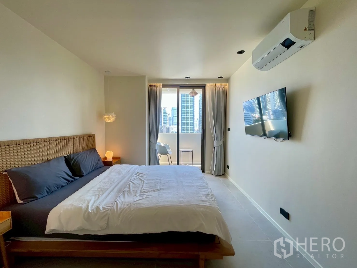 Condominium for sale in Watthana, Bangkok - Sunlit bedroom with king bed, wall-mounted TV, and balcony city skyline view.