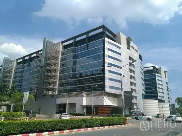 Office Space for rent in Pak Kret, Nonthaburi - Exterior of a contemporary glass-fronted office complex with wide road and parking.