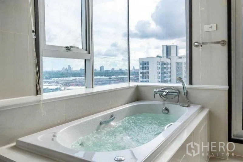 房间 出租在Khlong Toei, Bangkok - 转角浴缸注水中，落地窗外是曼谷城市天际线。