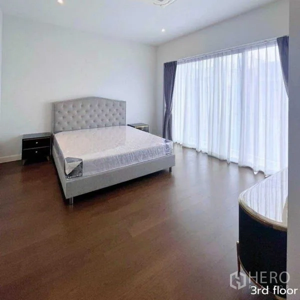 Detached House for rent in Bang Kapi, Bangkok - Bright bedroom with wood floors and floor-to-ceiling curtains opening to balcony.