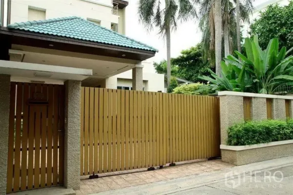 Detached House for rent in Phaya Thai, Bangkok - Street-side view of the home’s wooden gate, green tiled roof and lush palms along the boundary wall.
