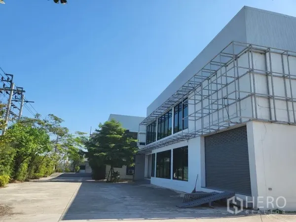 คลังสินค้า ขายในLat Krabang, Bangkok - มุมอาคารโกดังสีขาว หน้าต่างบานใหญ่ ประตูกลิ้ง โครงกันสาด และลานคอนกรีตกว้าง