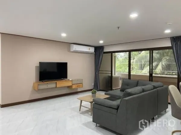 公寓 出租或出售在Watthana, Bangkok - 开放式客厅，灰色转角沙发、墙挂电视与通往阳台的落地推拉门。